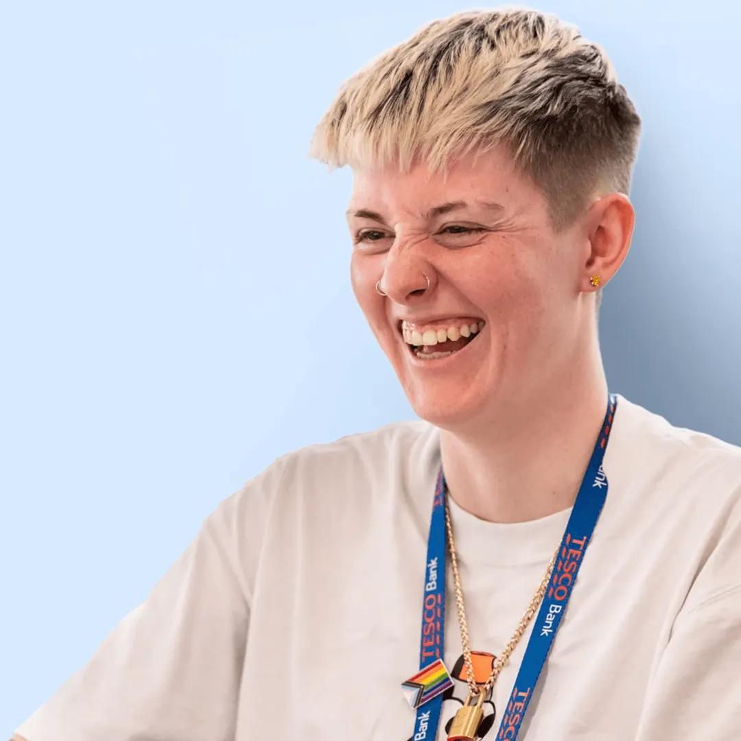 A smiling Tesco Bank colleague with a branded lanyard in front of a vibrant blue backdrop.