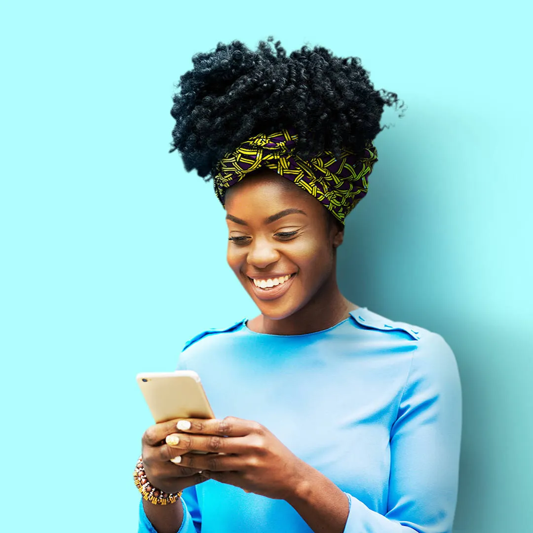 Joyful Black woman in a blue top, hair in a yellow-black wrap, smiling brightly at her phone, representing control functions.