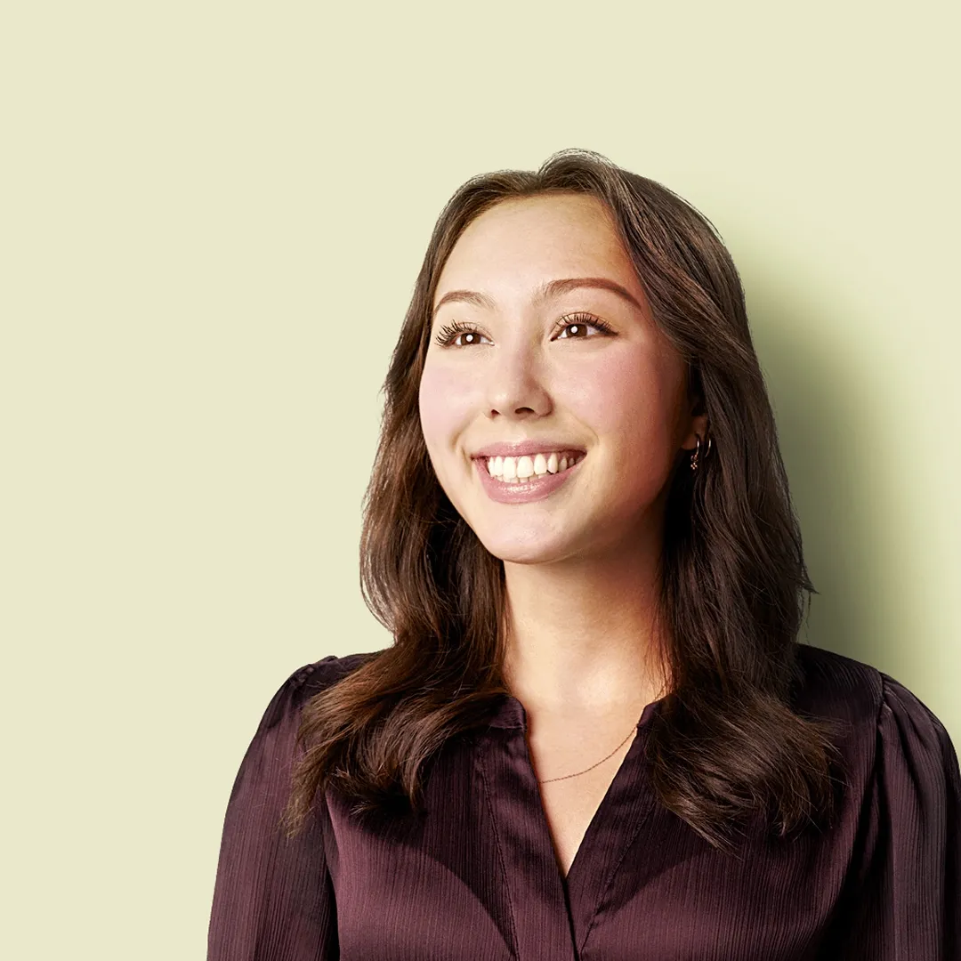 Smiling young Asian woman with long dark hair and shiny brown shirt, eyes bright, conveying optimism and helpfulness in customer service.