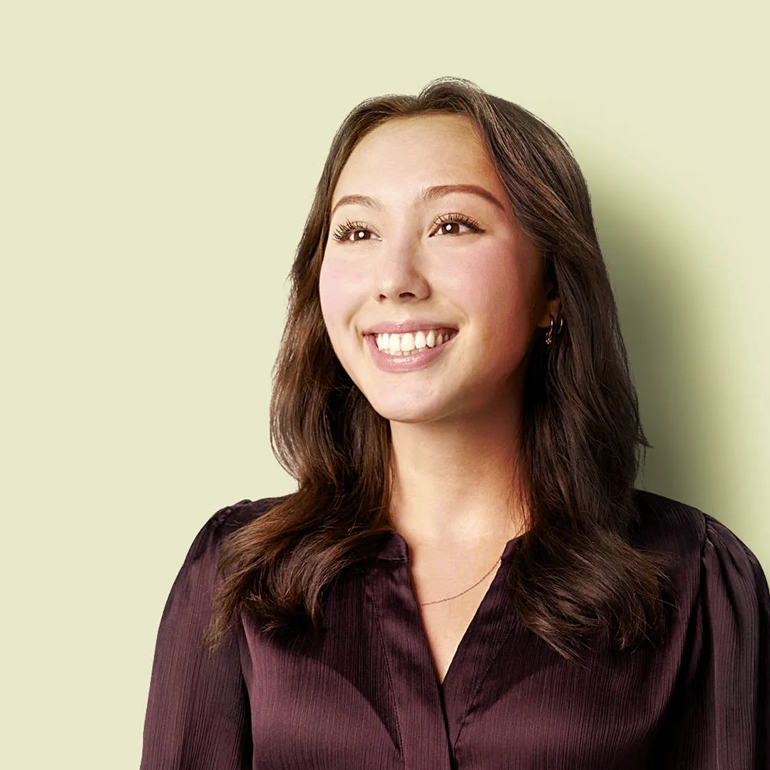Smiling young Asian woman with long dark hair and shiny brown shirt, eyes bright, conveying optimism and helpfulness in customer service.